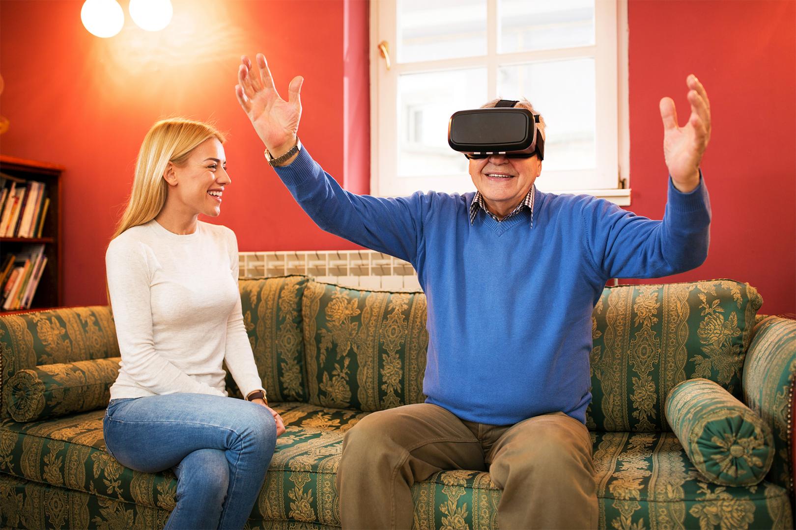 Frau und Rentner mit VR-Brille auf Sofa sitzend
